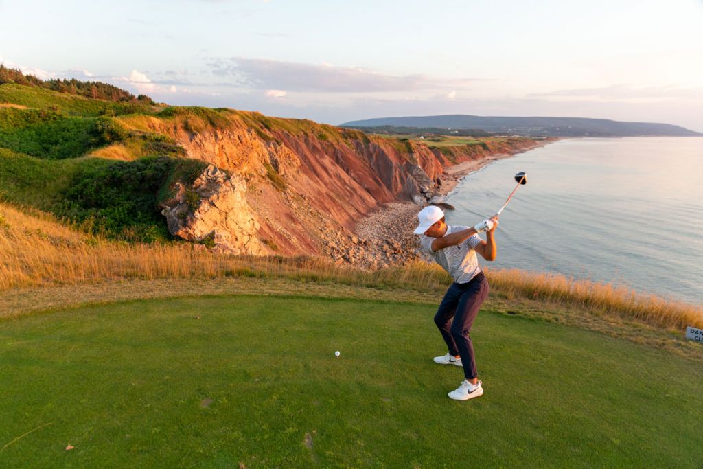 Golfer teeing off above coastal cliffs in Cape Breton