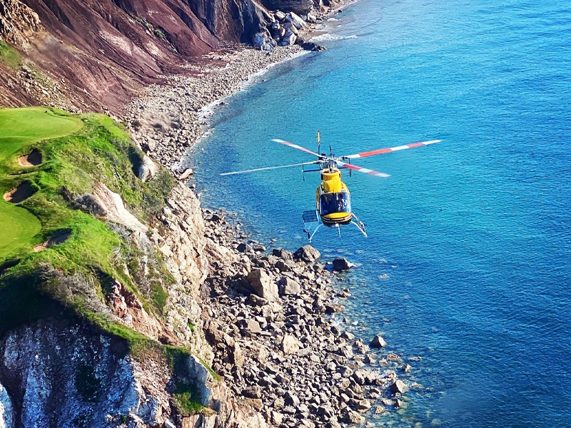 Helicopter flying along Cape Breton coastline over turquoise ocean