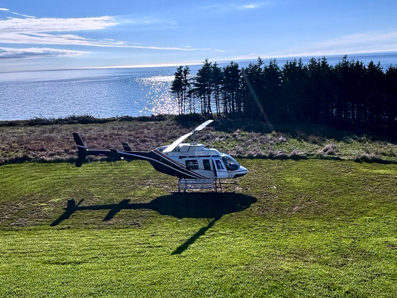 Helicopter landing in grassy field during Cape Breton private charter experience